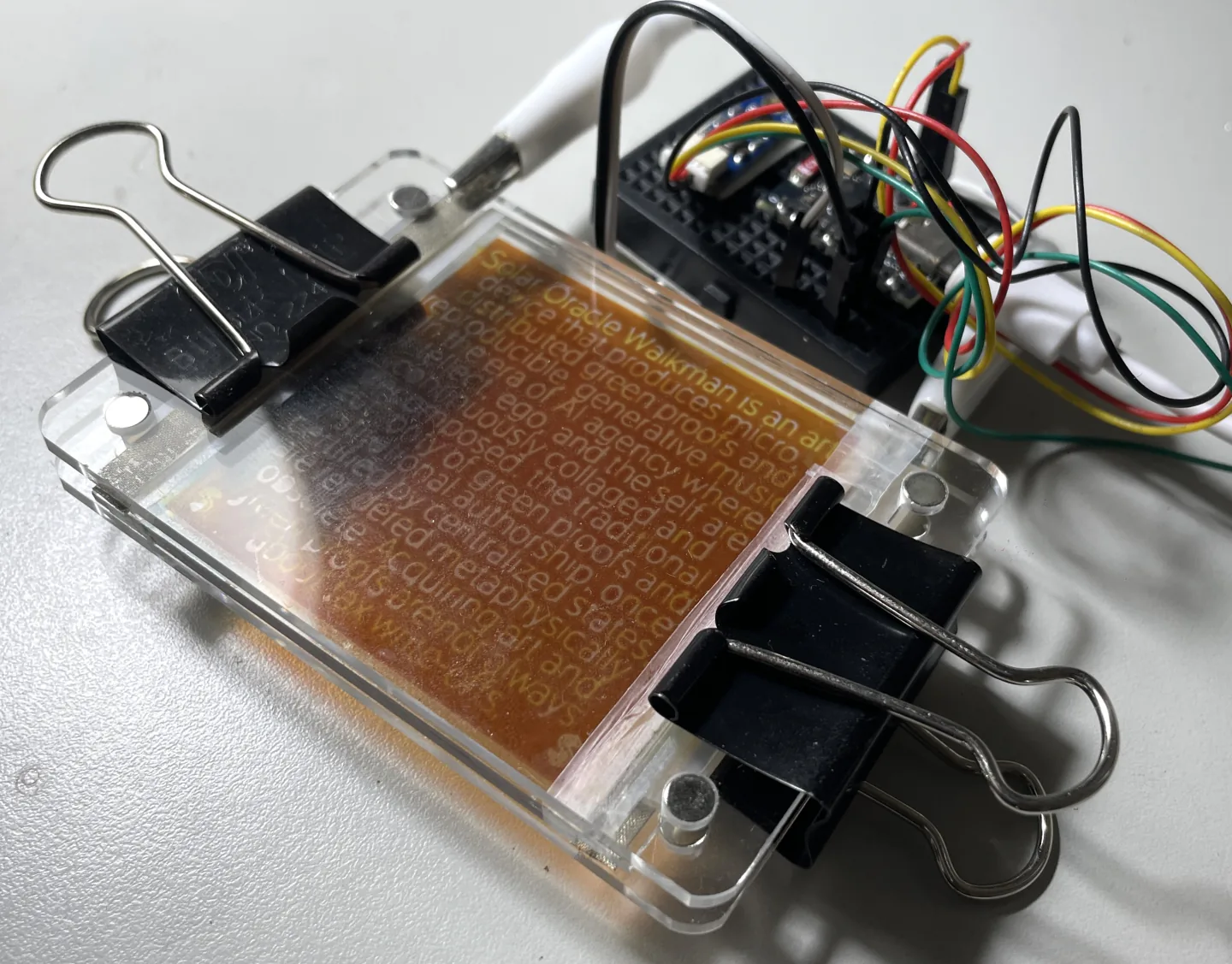 A handmade DSSC held in an acrylic frame beside its sensor and ESP32 board